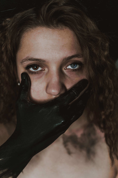 Black painted hand covering mouth of woman with terrified eyes and black mascara